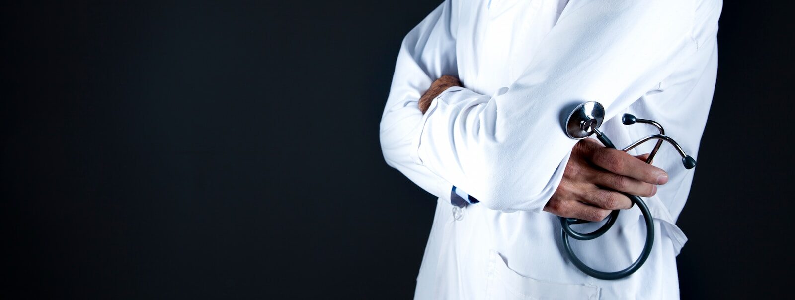 A person in a white lab coat holding a stethoscope against a dark background